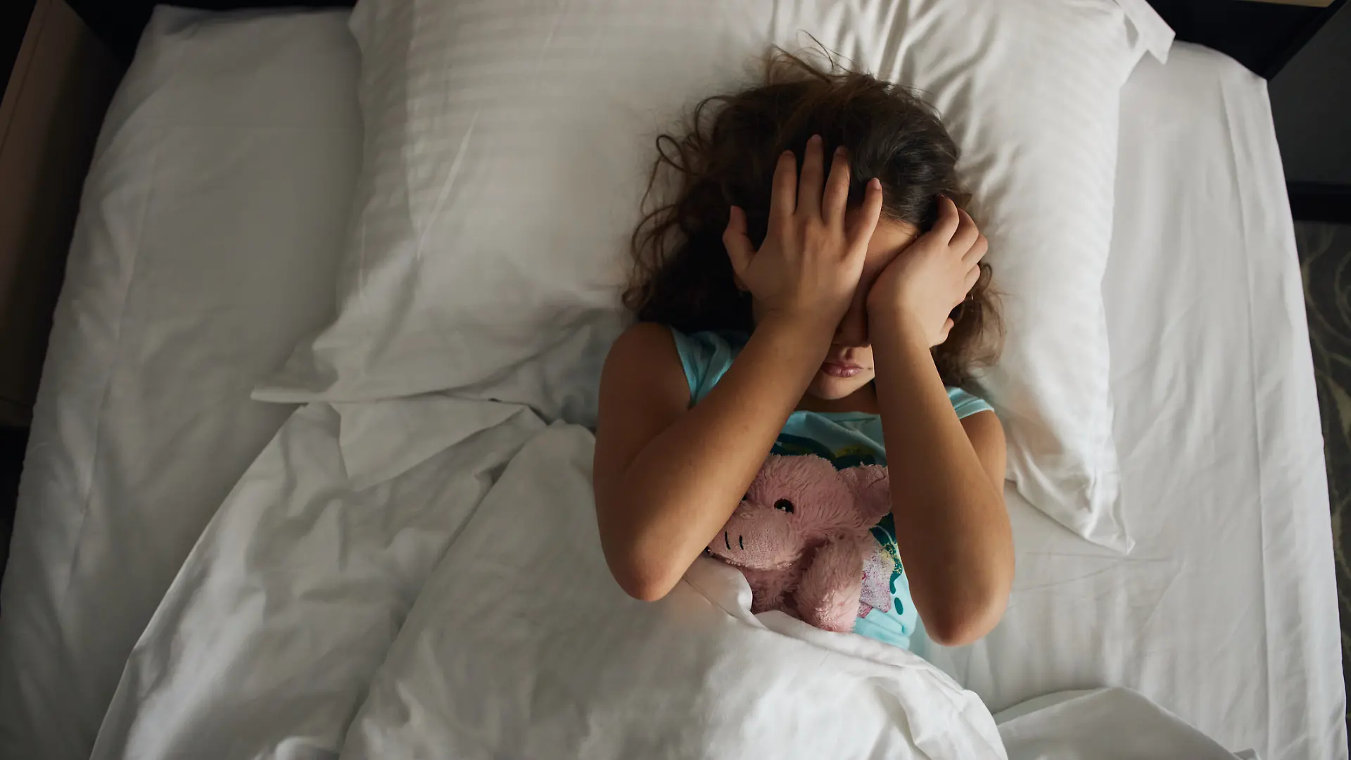 Ein Mädchen liegt morgens im Bett und wirkt müde.