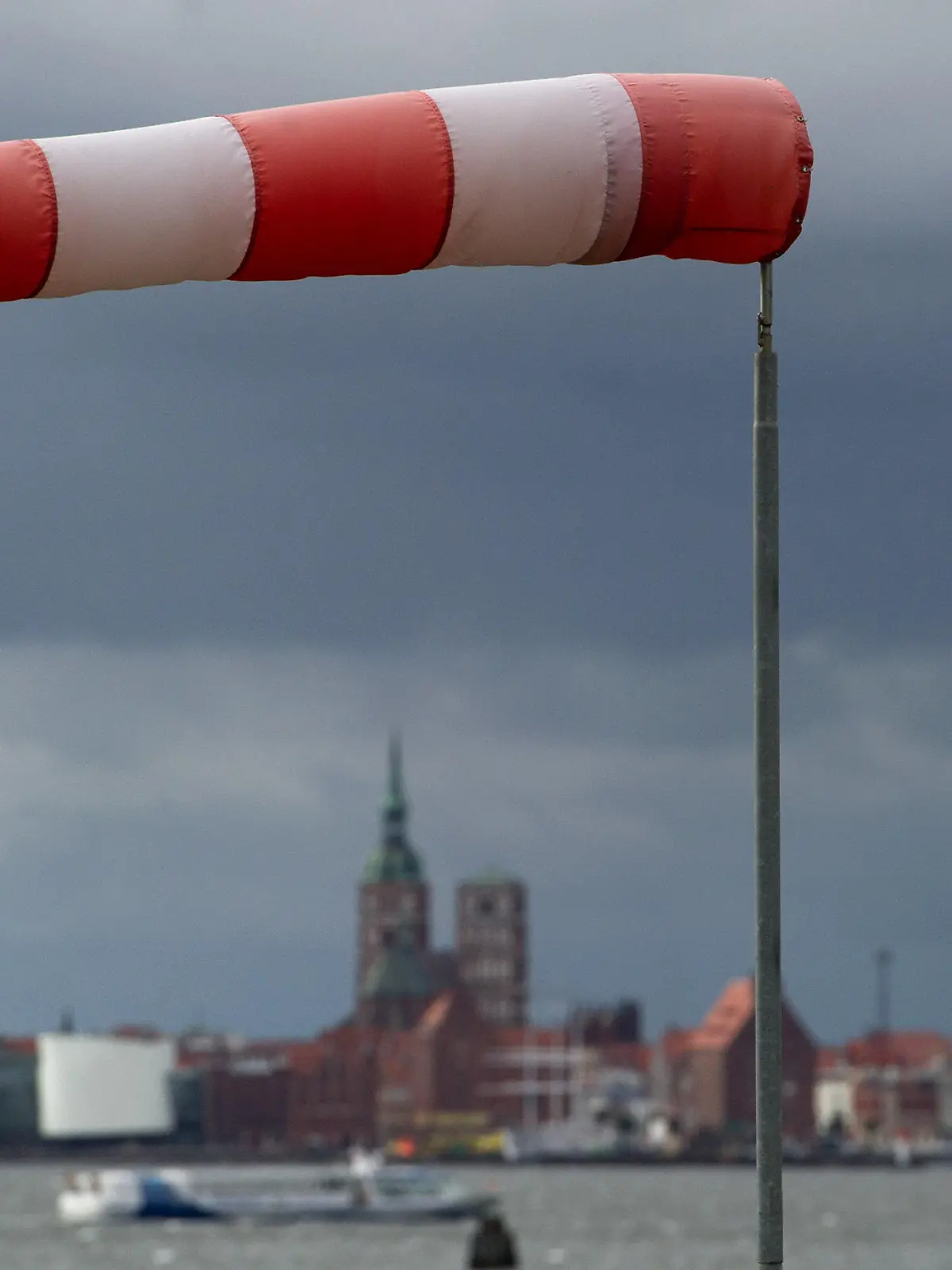 Ein Windsack steht fast horizontal in der Luft und zeigt somit recht starken Wind an, aufgenommen am 22.09.2014 in Altefähr (Mecklenburg-Vorpommern) an der Rügenbrücke auf der Insel Rügen, im Hintdergrund die Silhouette der Hansestadt Stralsund. Foto: Stefan Sauer/dpa +++(c) dpa - Bildfunk+++