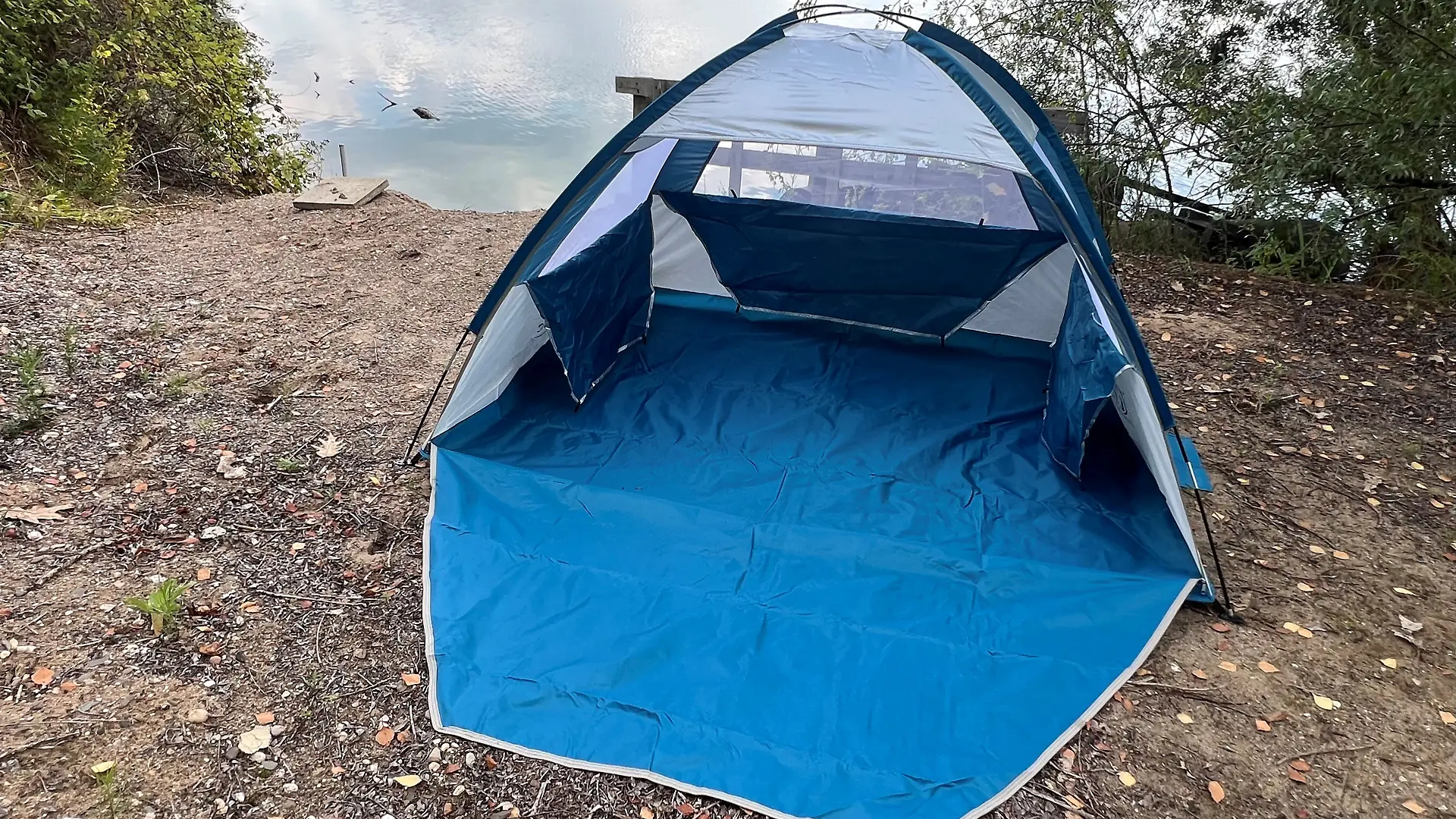 Die blaue Strandmuschel von COMMOUDS ist aufgebaut. Im Hintergrund sieht man einen See. 