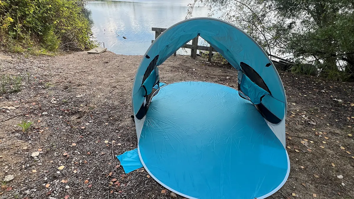 Die blaue Strandmuschel von WolfWise ist aufgebaut. Im Hintergrund sieht man einen See. 