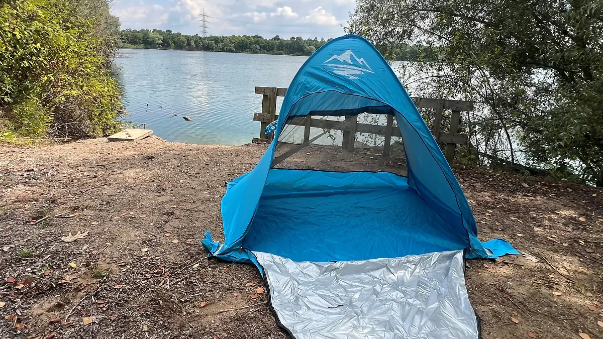 Die blaue Strandmuschel von Purebox ist aufgebaut. Im Hintergrund sieht man einen See. 