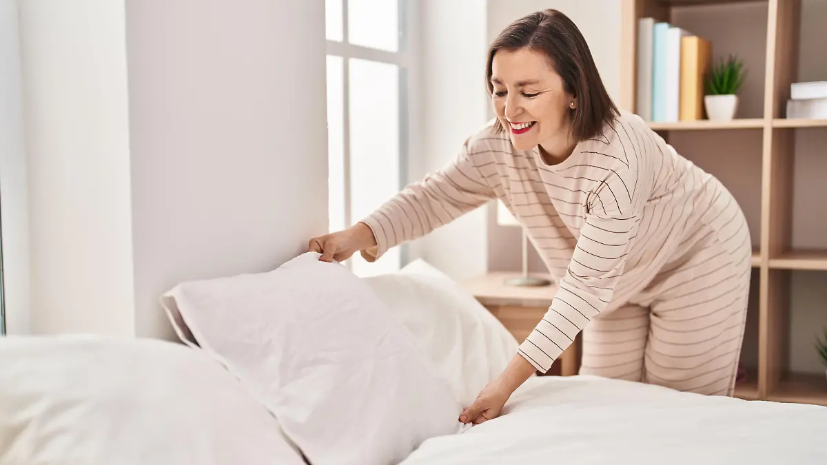 Middle age woman making bed standing at bedroom