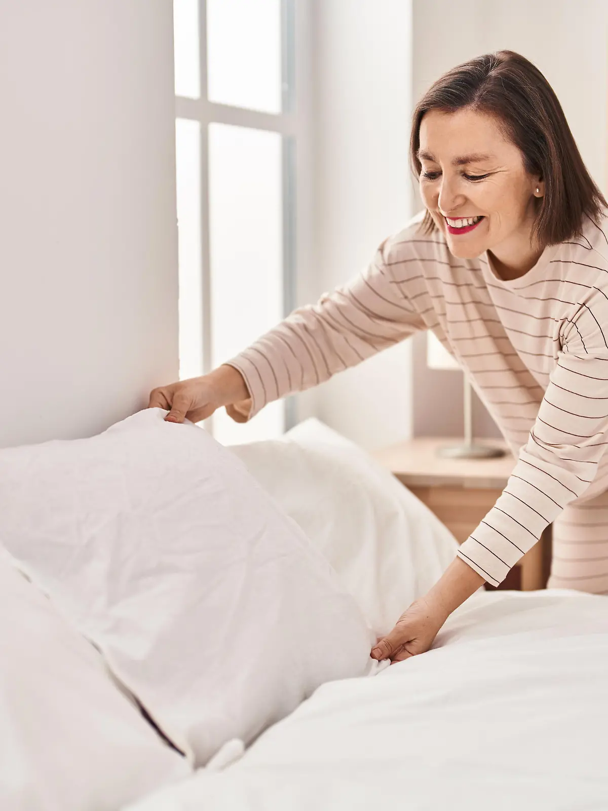 Middle age woman making bed standing at bedroom