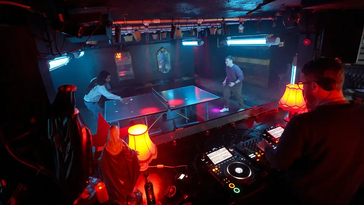 PRODUKTION - 05.01.2023, Hamburg: Julius (hinten r) und Kevin (hinten l) spielen Tischtennis zu wuchtigen Techno-Beats von DJ Larzo (vorne r) während der wöchentlichen Veranstaltung ·Topspin Techno· im Solar Club im Baalsaal auf der Reeperbahn. Techno, Tischtennis, Topspin - was als Idee für ein oder zwei Events startete, hat sich mittlerweile in der Hamburger Techno-Szene fast schon als Pflichttermin an Donnerstagen entwickelt. Wer Lust auf Tischtennis-Rundlauf und Sets von Hamburger DJs hat ist bei Topspin auf jeden Fall an der richtigen Adresse. (zu dpa ·Topspin Techno - Tischtennis im Szeneclub·) Foto: Marcus Brandt/dpa +++ dpa-Bildfunk +++