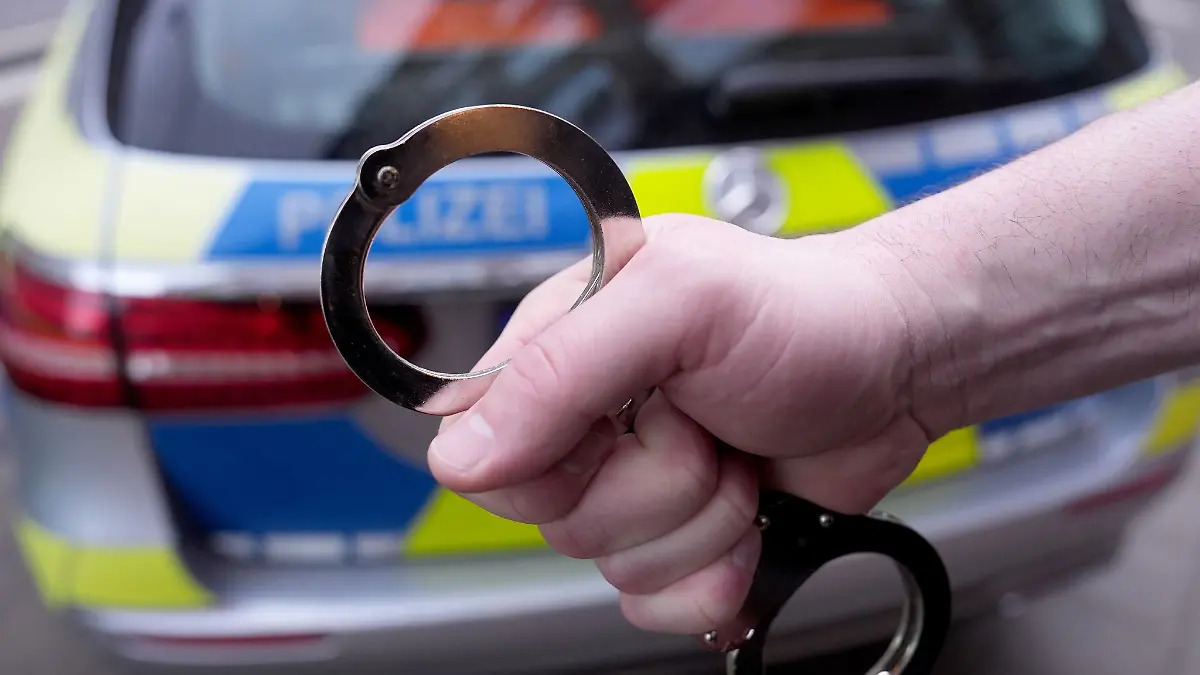 Handschellen vor einem Polizei-Auto