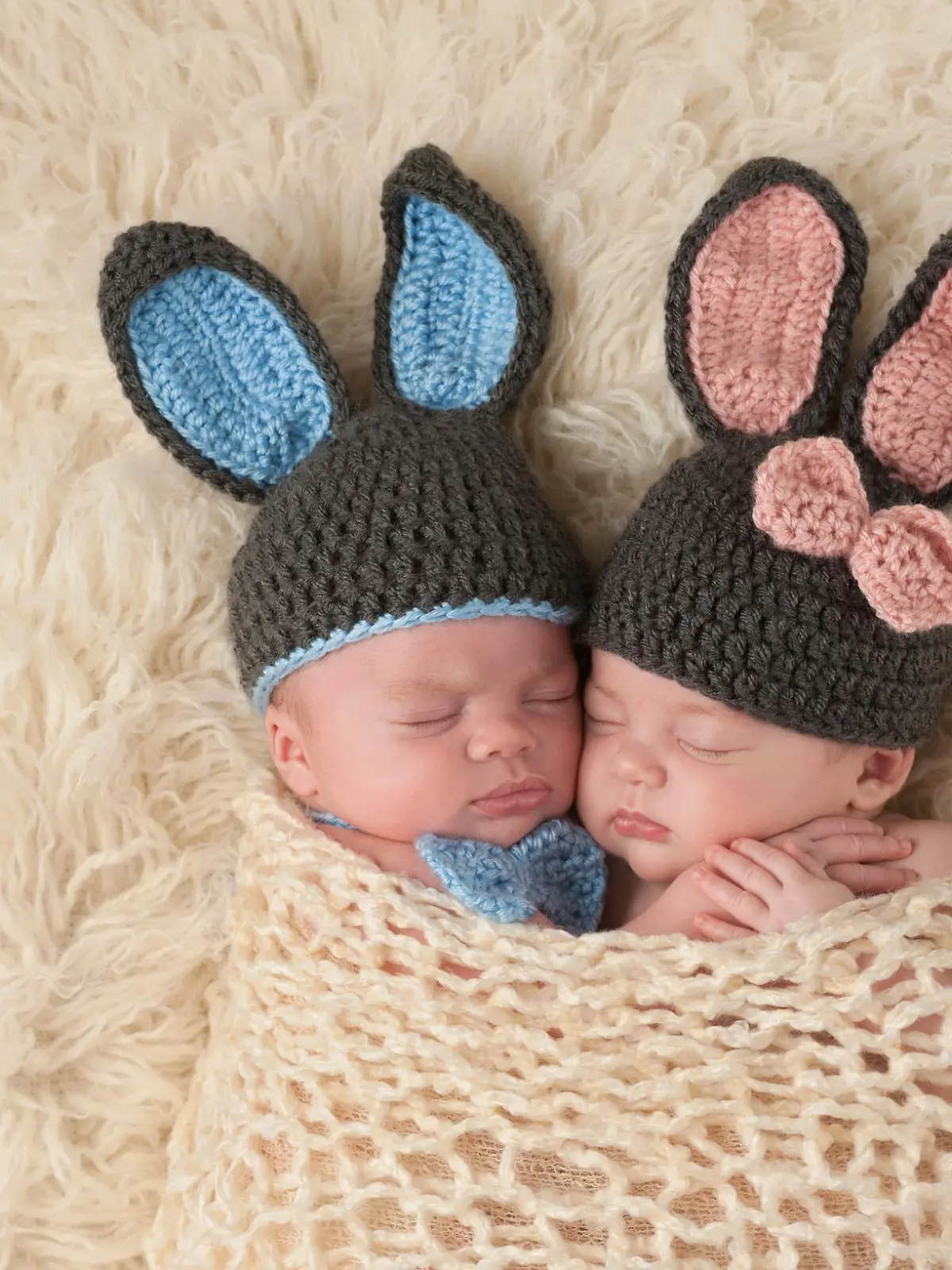Sleeping 2 month old newborn baby twins wearing bunny costumes. They are swaddled together in a hugging position.
