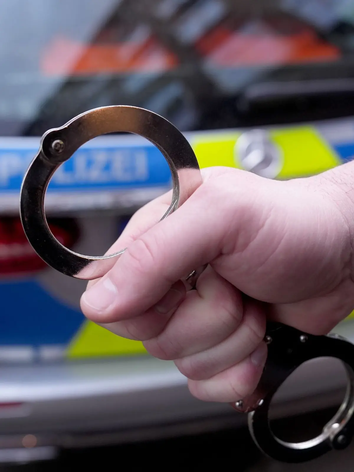 Handschellen vor einem Polizeiauto
