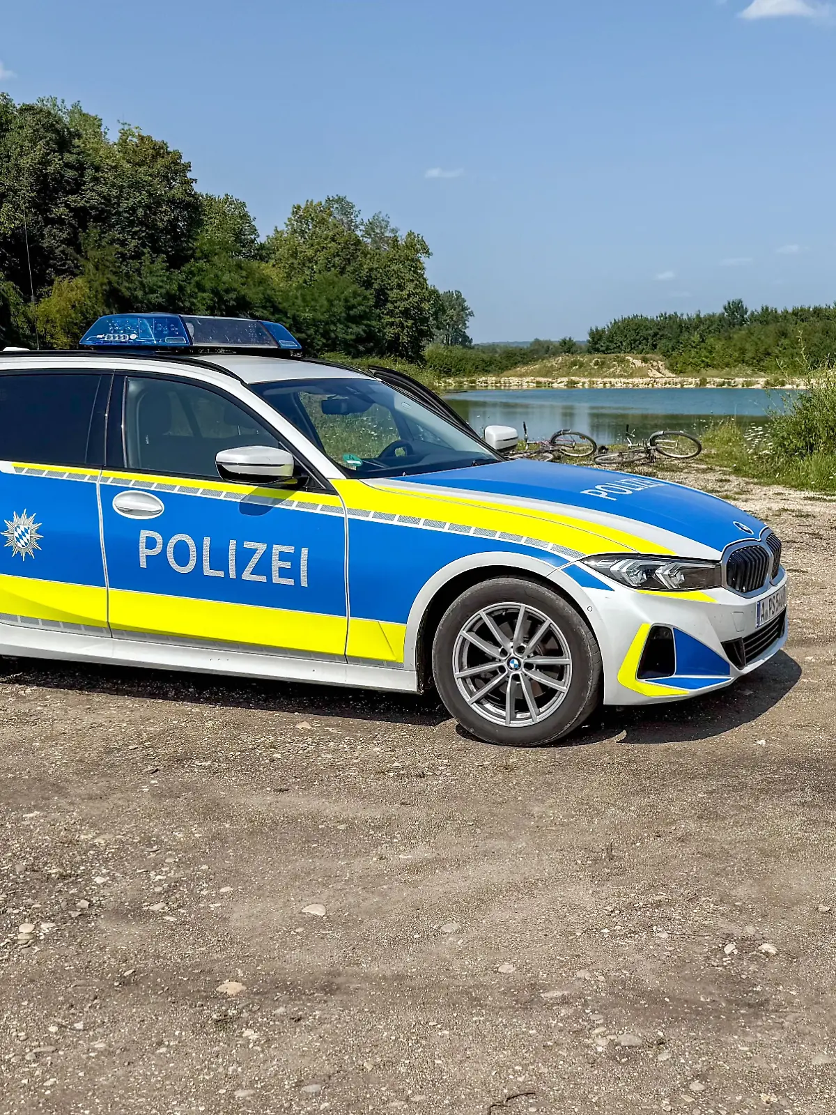 Ein Polizeiauto steht vor einem Badesee. 