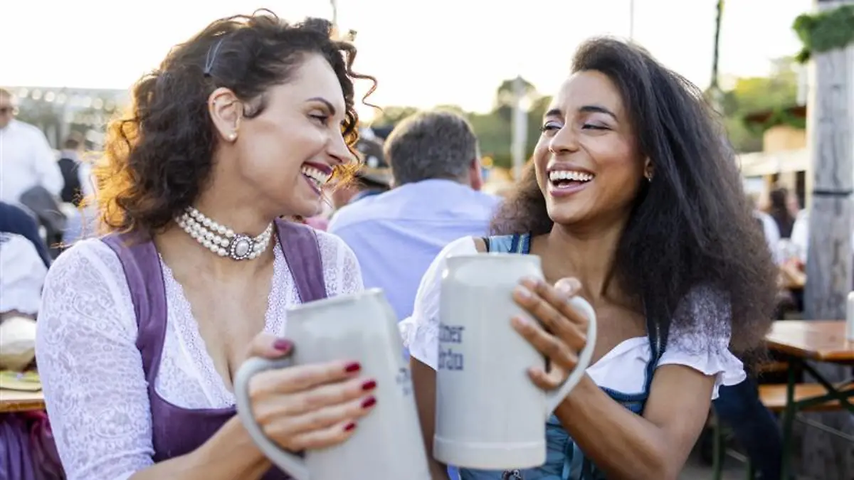 Zwei Freundinnen tragen Trend-Dirndl und stoßen mit Bier an.
