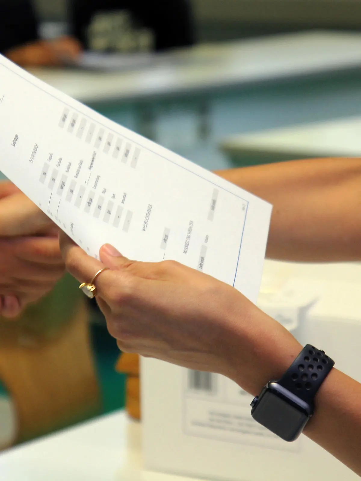 Eine Lehrerin eines Gymnasiums steht am letzten Schultag vor den Sommerferien mit einem Zeugnis in der Hand in einem Klassenzimmer und schüttelt einer Schülerin bei der Zeugnisübergabe die Hand.