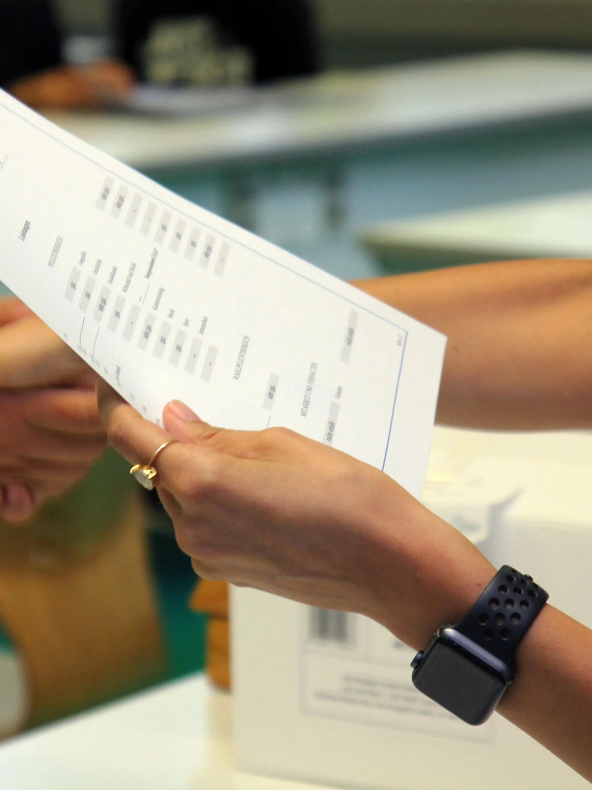 Eine Lehrerin eines Gymnasiums steht am letzten Schultag vor den Sommerferien mit einem Zeugnis in der Hand in einem Klassenzimmer und schüttelt einer Schülerin bei der Zeugnisübergabe die Hand.