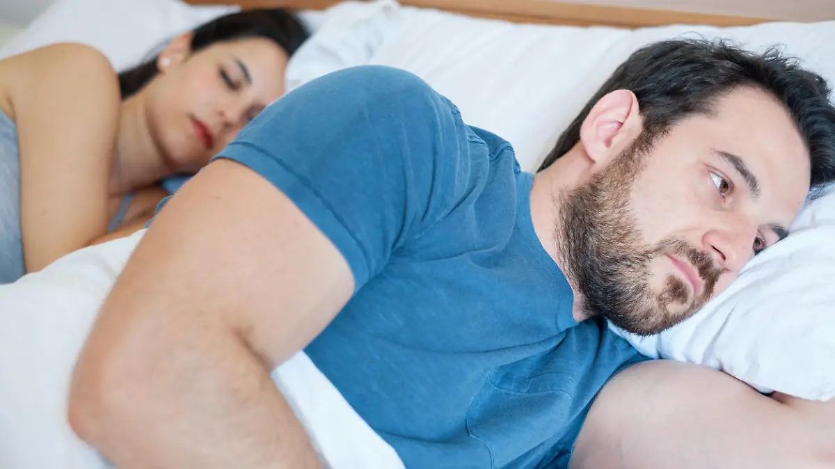Depressed young man lying in bed and having problems with his girlfriend