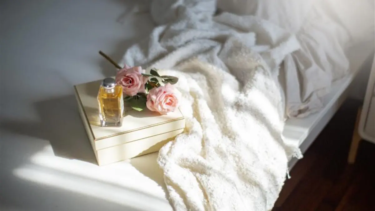 Rosen-Parfum, Bouquet und Karton auf einem Bett.