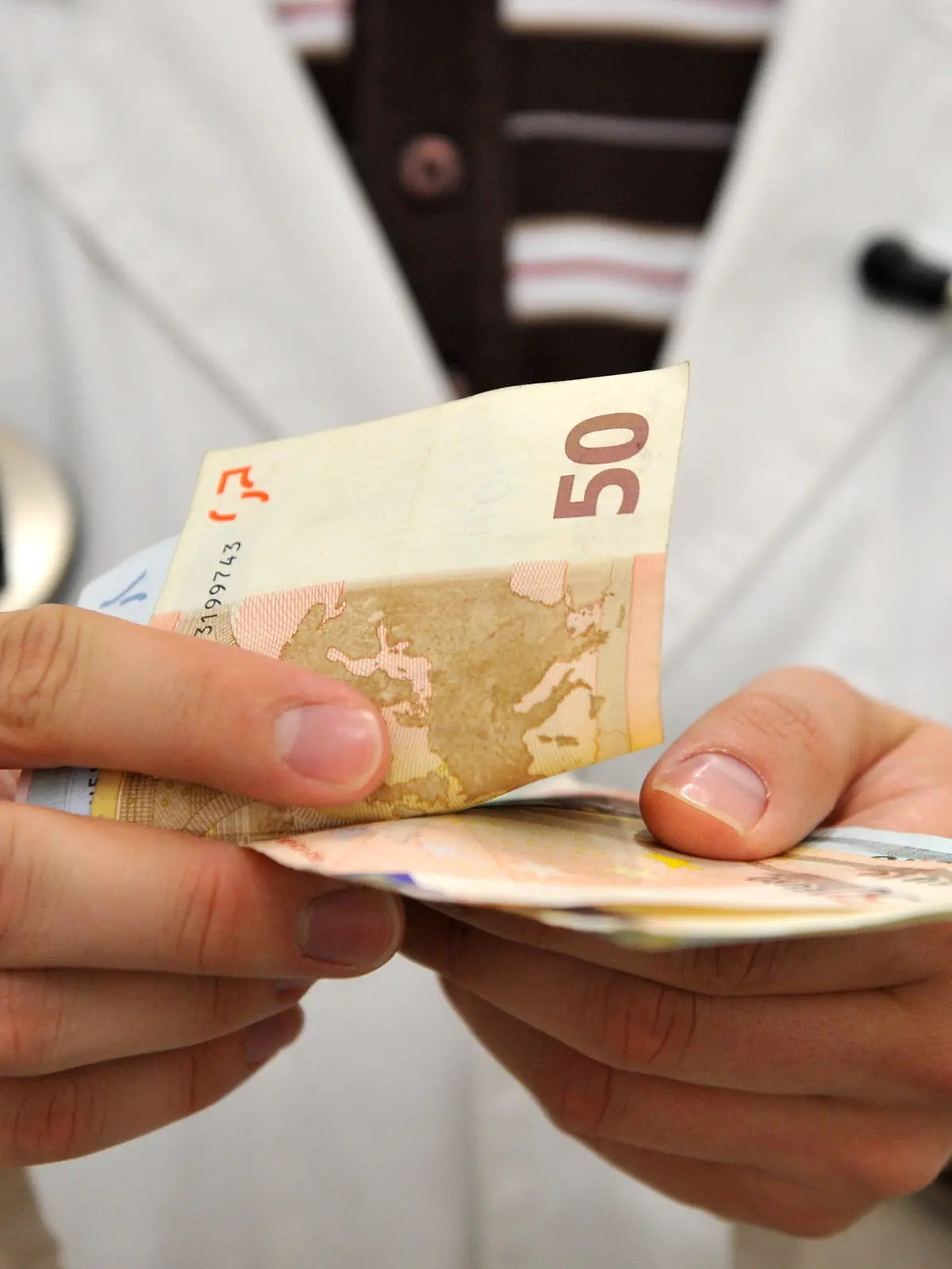 ARCHIV - ILLUSTRATION - Ein Mann im Arztkittel zählt am 03.09.2009 Geldscheine. Die gesetzlichen Krankenkassen registrieren eine zunehmende Zahl von Privatpatienten, die wieder zu ihnen zurückkehren wollen. «Bei uns häufen sich die telefonischen Anfragen von Privatversicherten, die zur AOK kommen wollen», sagte der Chef der AOK Rheinland/Hamburg, Wilfried Jacobs, dem «Spiegel».  Foto: Tobias Hase dpa  +++(c) dpa - Bildfunk+++