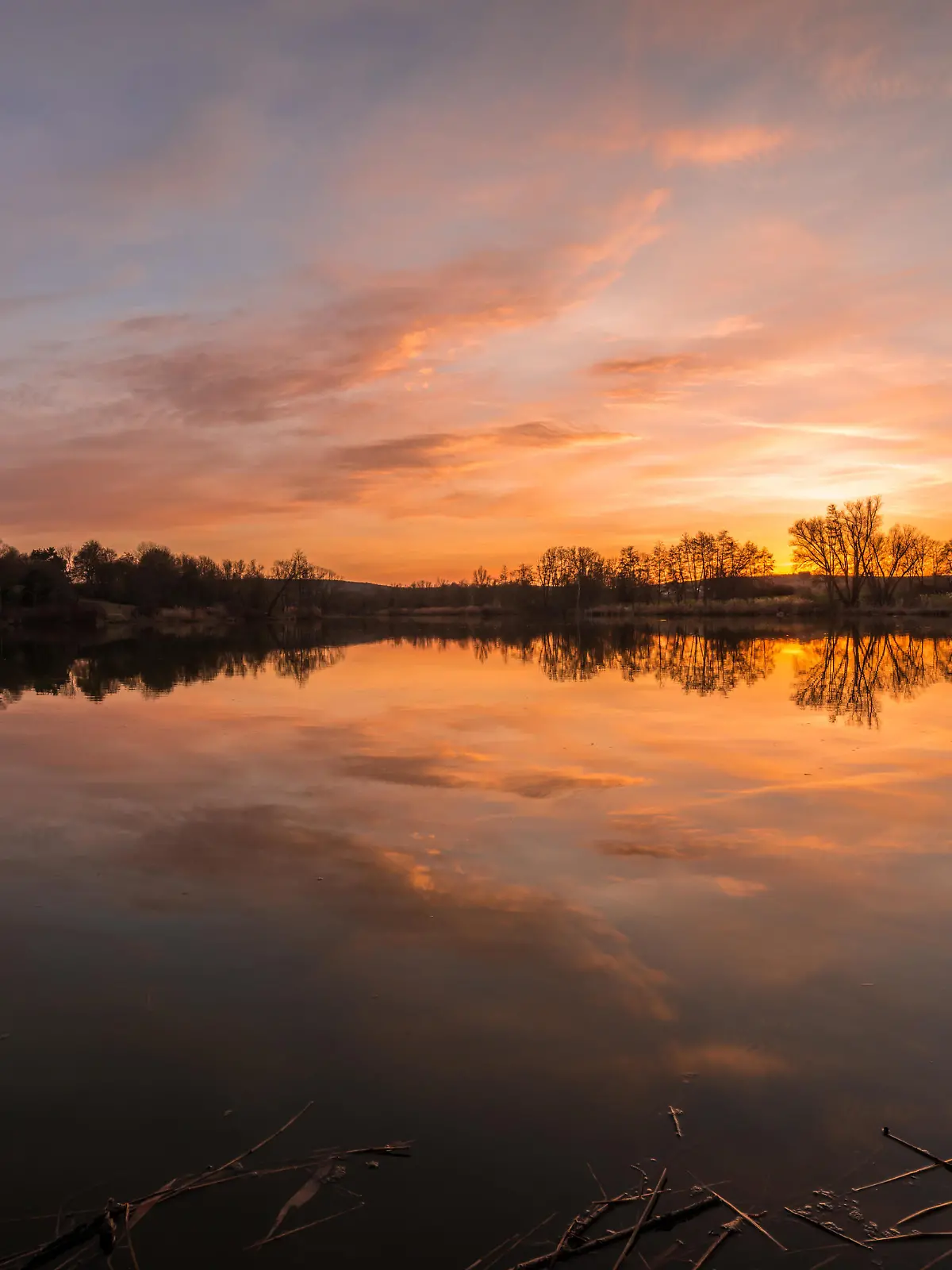 Landscape and sunset on the shore in Westpark Donaupark in Regensburg with reflection of sky in the smooth lake with beautiful dramatic play of colors play with clouds, Germany