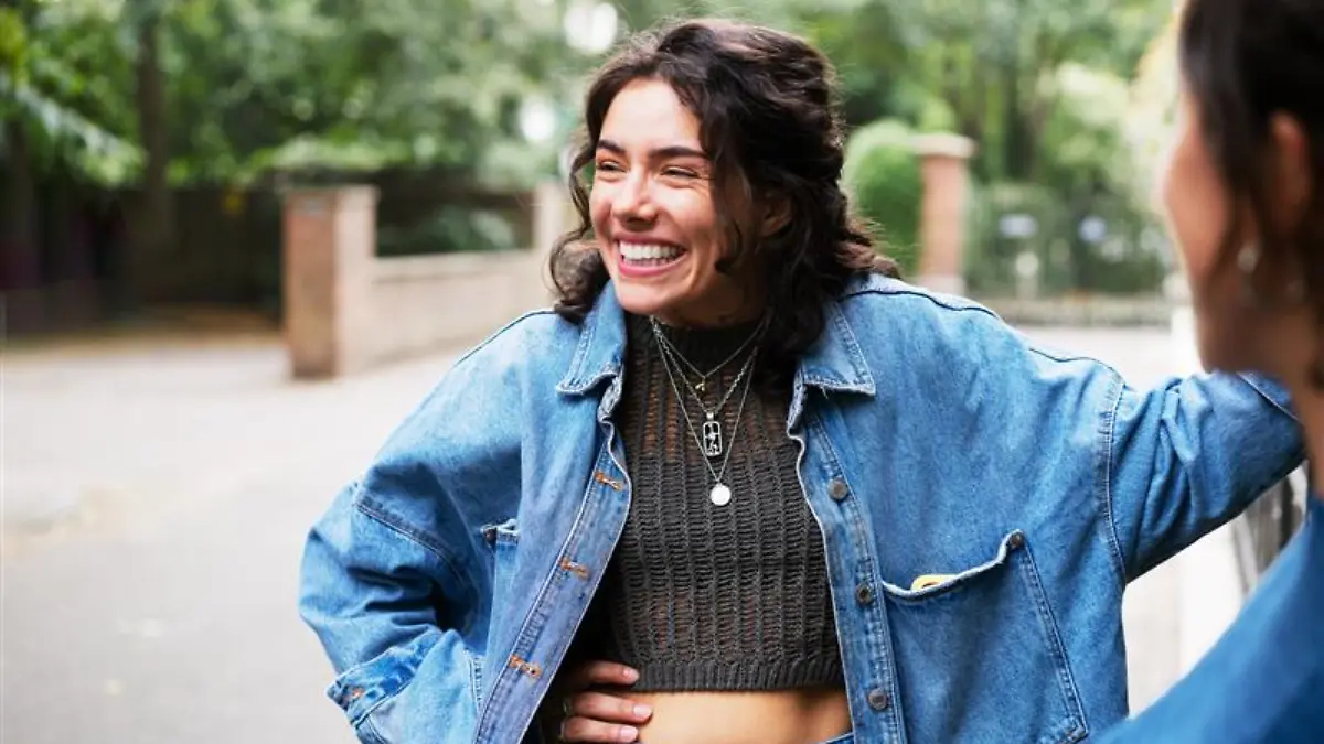 Lächelnde Frau in Oversized-Jeansjacke und cropped Stricktop.