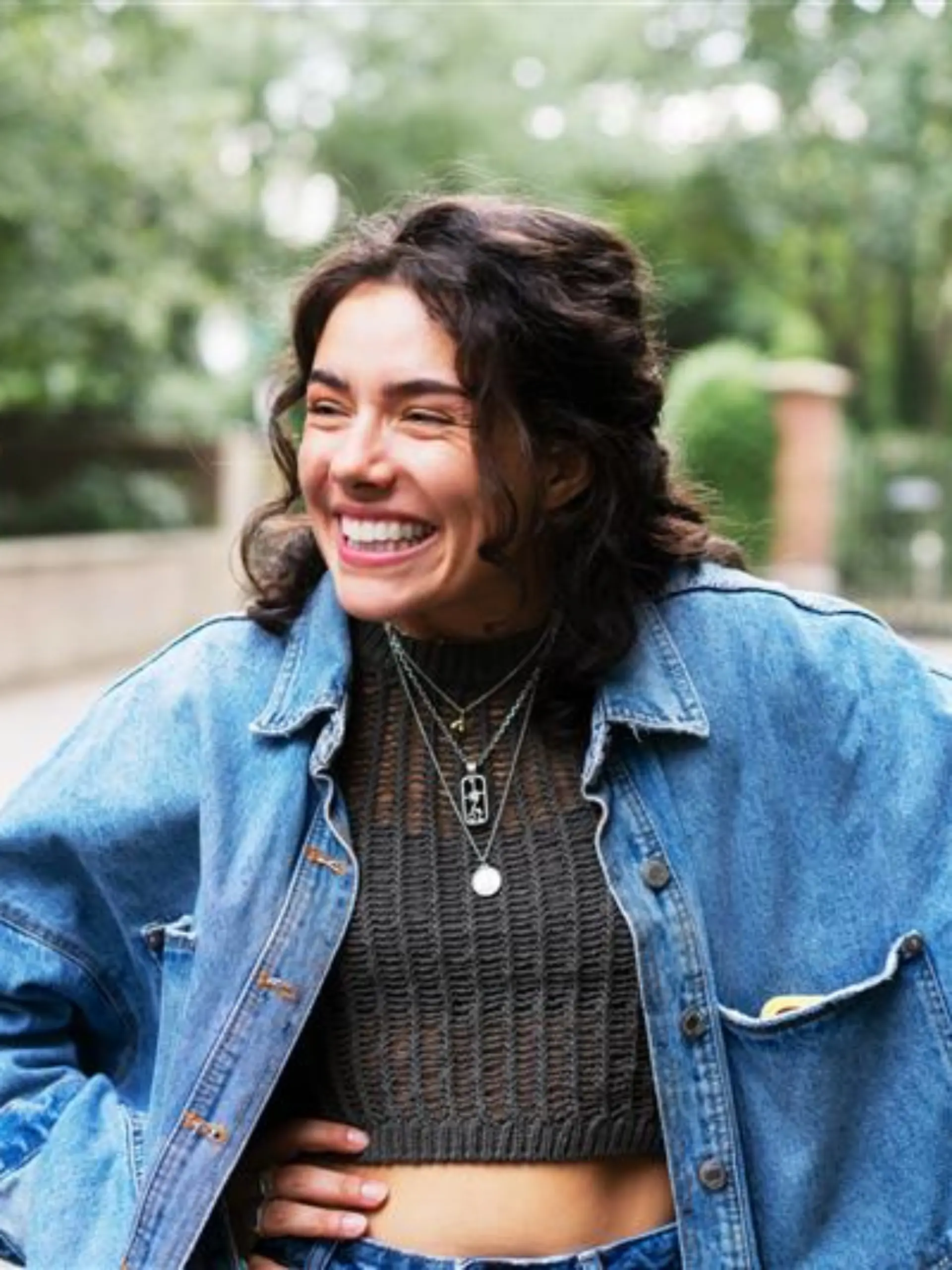 Lächelnde Frau in Oversized-Jeansjacke und cropped Stricktop.