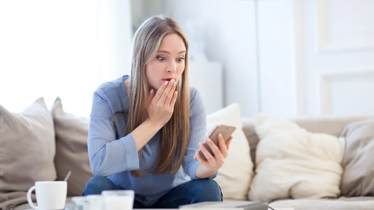 Eine junge Frau schaut erschrocken auf ihr Handy (gestellte Szene)