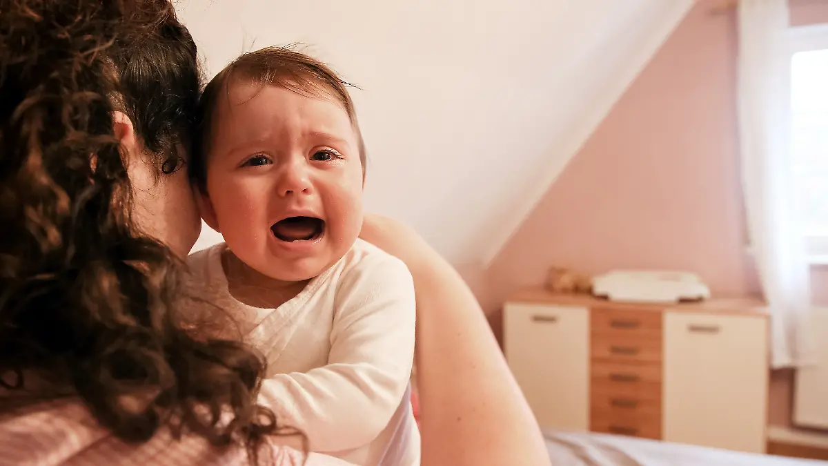 Eine junge Frau tröstet ihr weinendes Baby. 