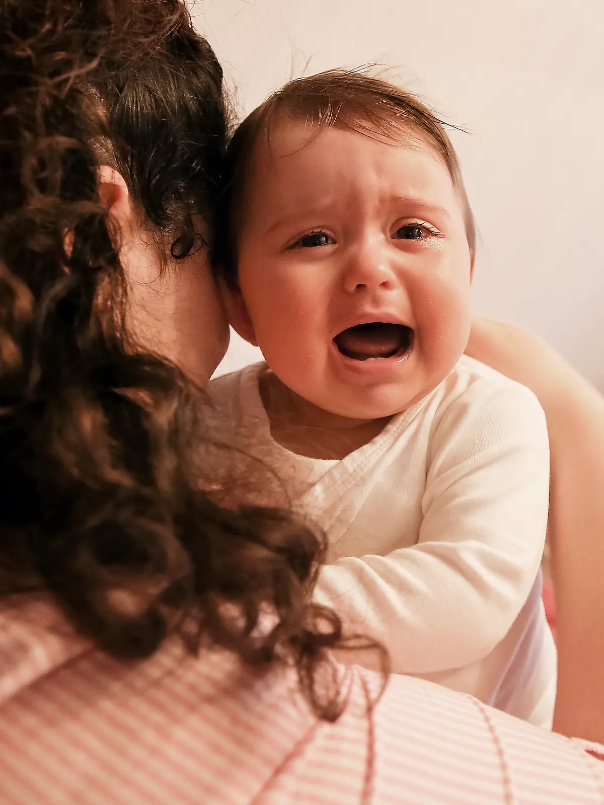 Eine junge Frau tröstet ihr weinendes Baby. 