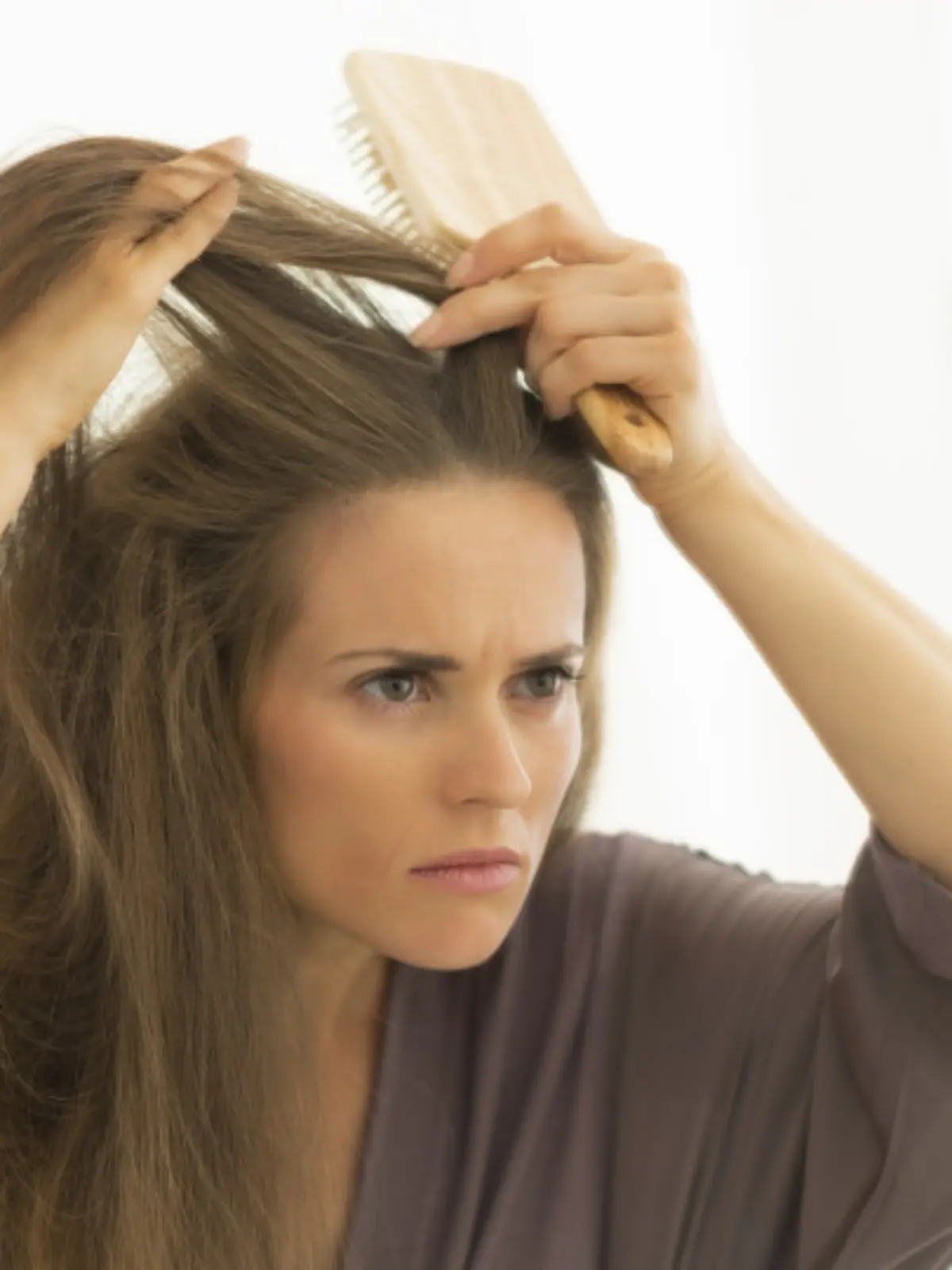 Concerned young woman combing hair in bathroom