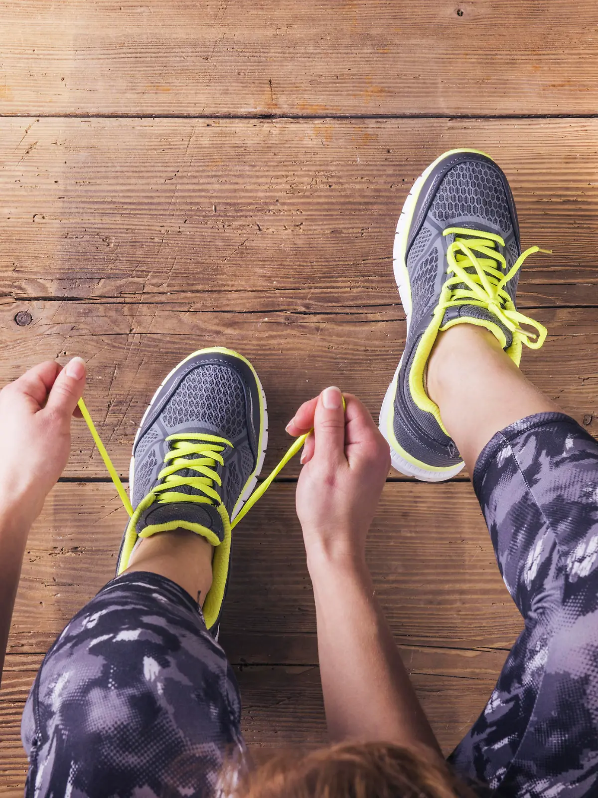 Unrecognizable young runner tying her shoelaces. Studio shot on wooden floor background.