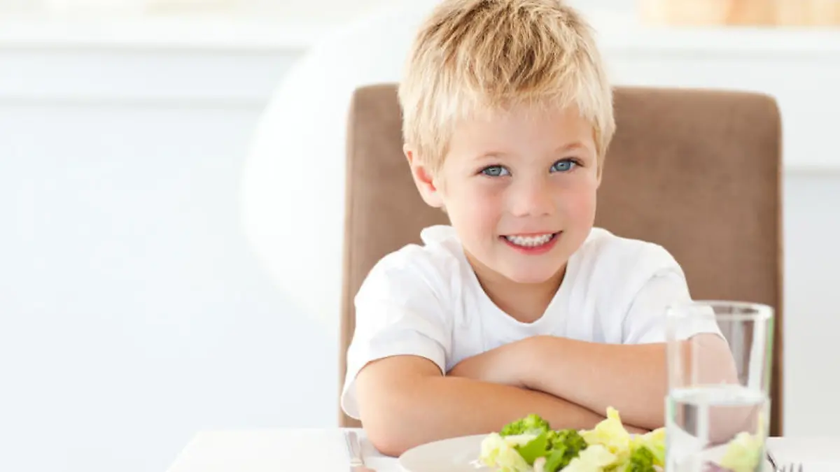 Portrait of a little boy eating a healthy salad for lunch in the kitchen