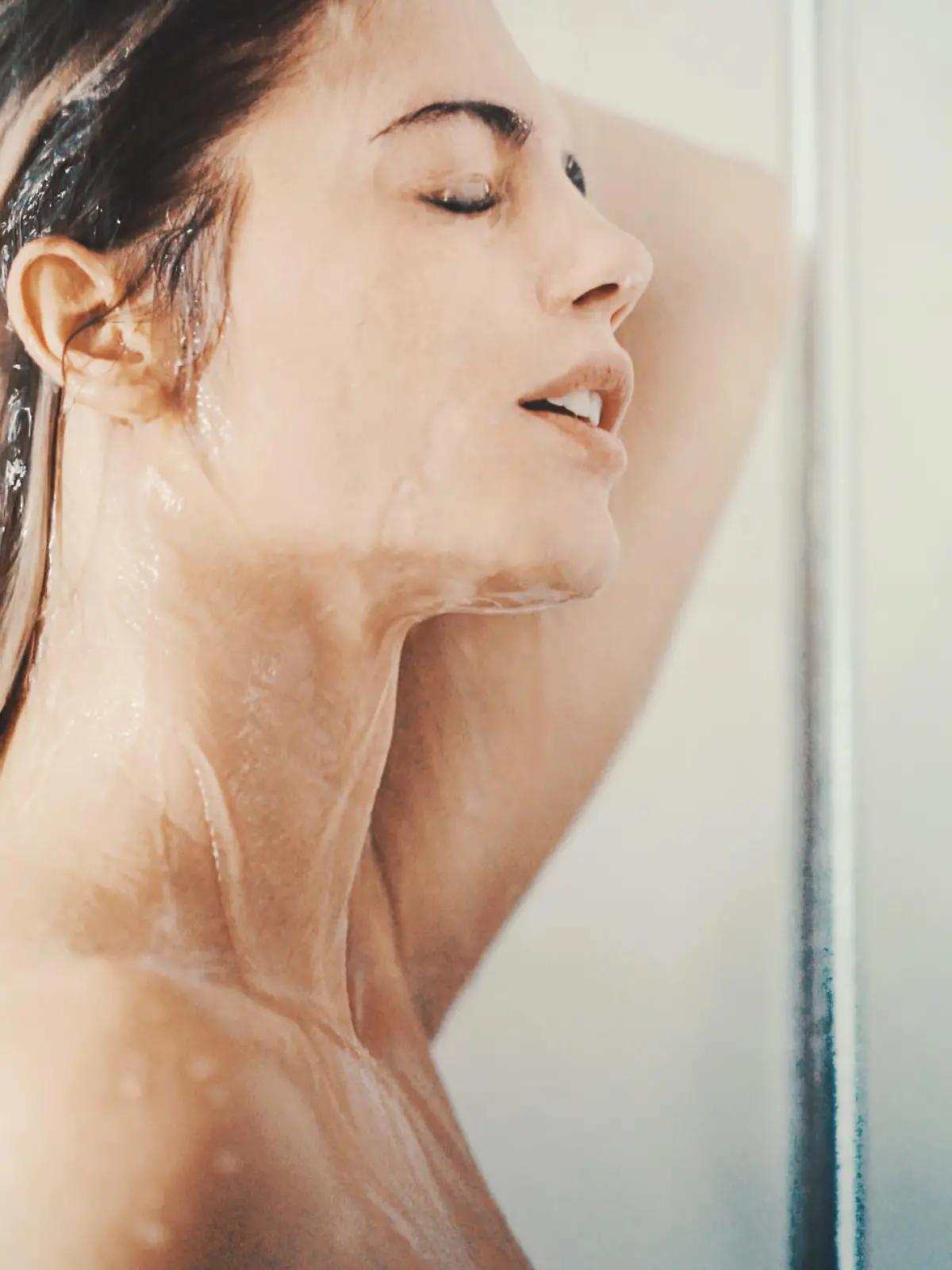 Closeup side view of mid 20's attractive woman taking a relaxing shower after a long stressful day. She's just standing under the waterflow without any soap or shampoo.