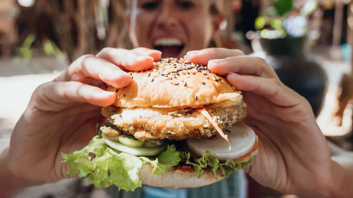 Girl in hipster cafe eating yummy burger. Tropical vacations, eating by the beach