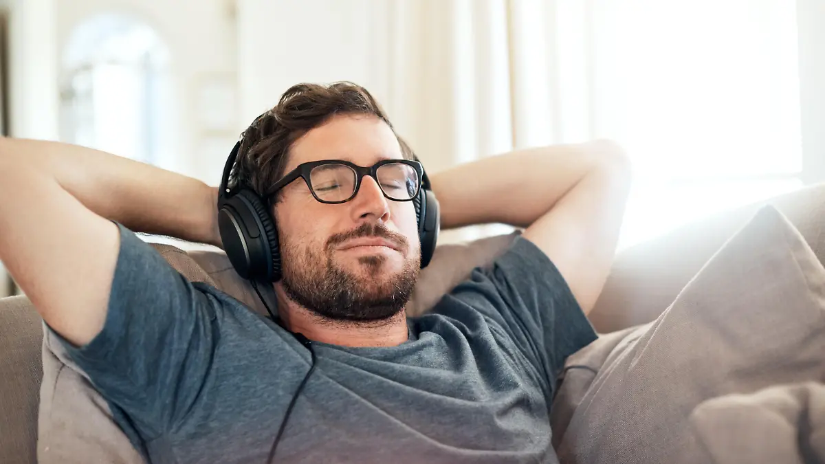 Cropped shot of a handsome young man listening to music on his tablet while relaxing on a sofa at home
