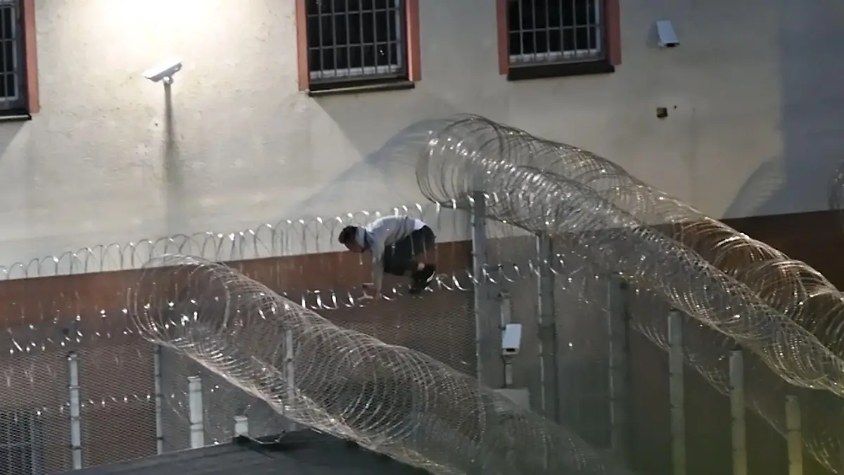 Hier büxt ein Häftling beinah aus – und alle schauen seelenruhig zu! Er quetscht sich durch Stacheldraht