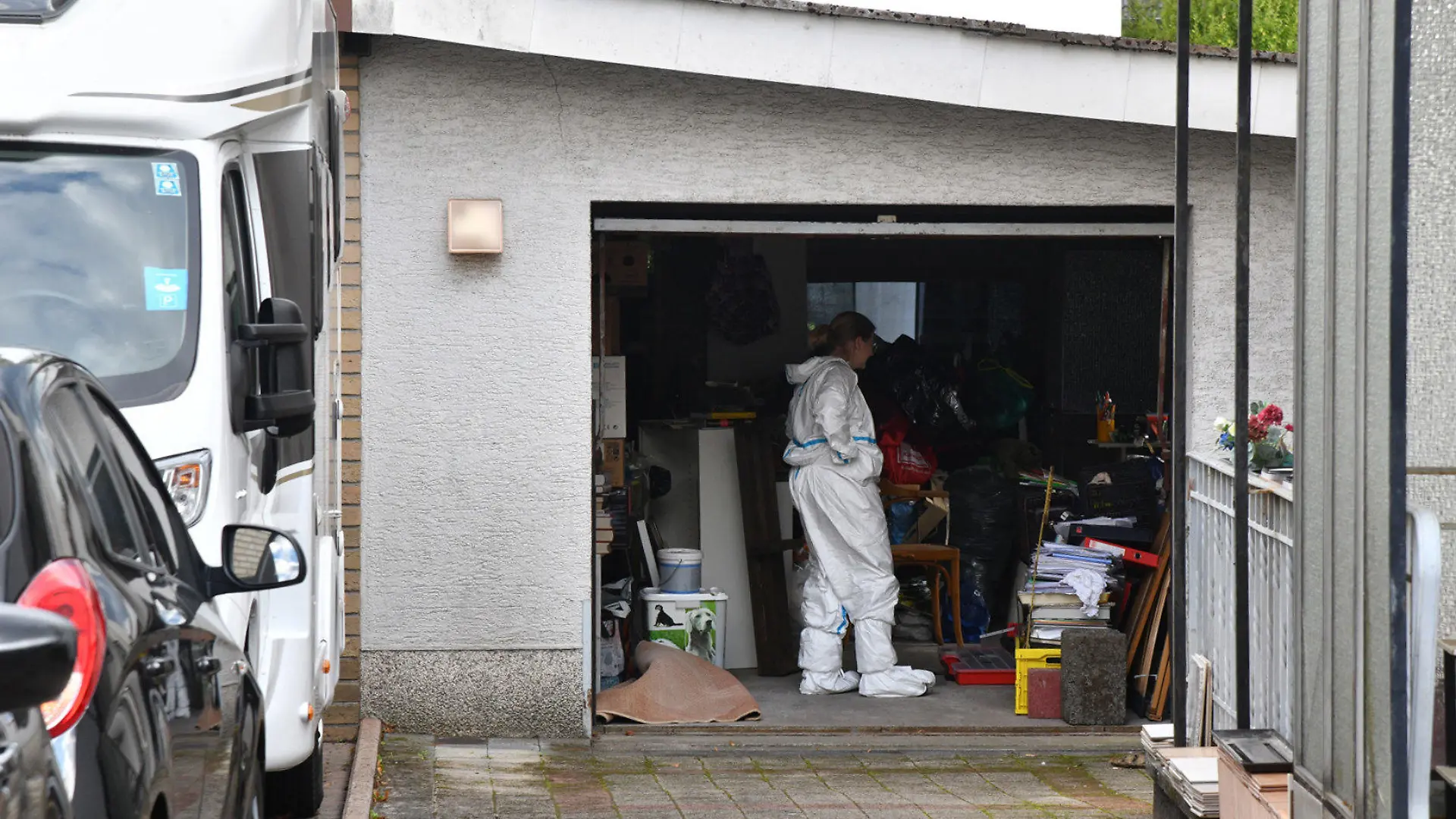 09.08.2023, Saarland, Homburg: Beamte durchsuchen eine Garage im Umfeld eines Gartens, in dem eine Leiche gefunden wurde. Eine verbuddelte Leiche ist im Garten eines Wohnhauses in Homburg (Saarpfalz-Kreis) entdeckt worden. Eine Nachbarin habe die Polizei verständigt, weil sie die Leiche gesehen habe, die bis auf die Füße in der Erde verbuddelt gewesen sei, sagte ein Polizeisprecher. Foto: Beckerbredel/BeckerBredel/dpa - ACHTUNG:Hausnummer gepixelt +++ dpa-Bildfunk +++