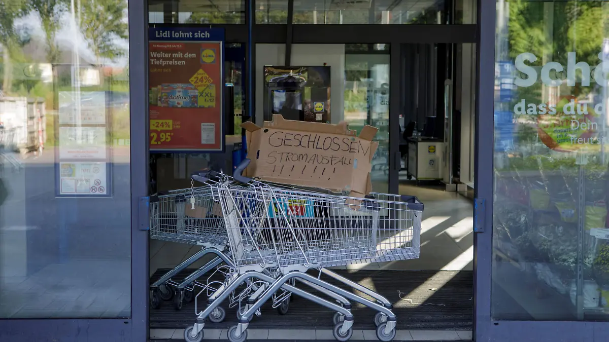 Im Eingang eines Supermarkts steht ein Einkaufswagen mit einer Pappe mit der Aufschrift „Geschlossen Stromausfall”.