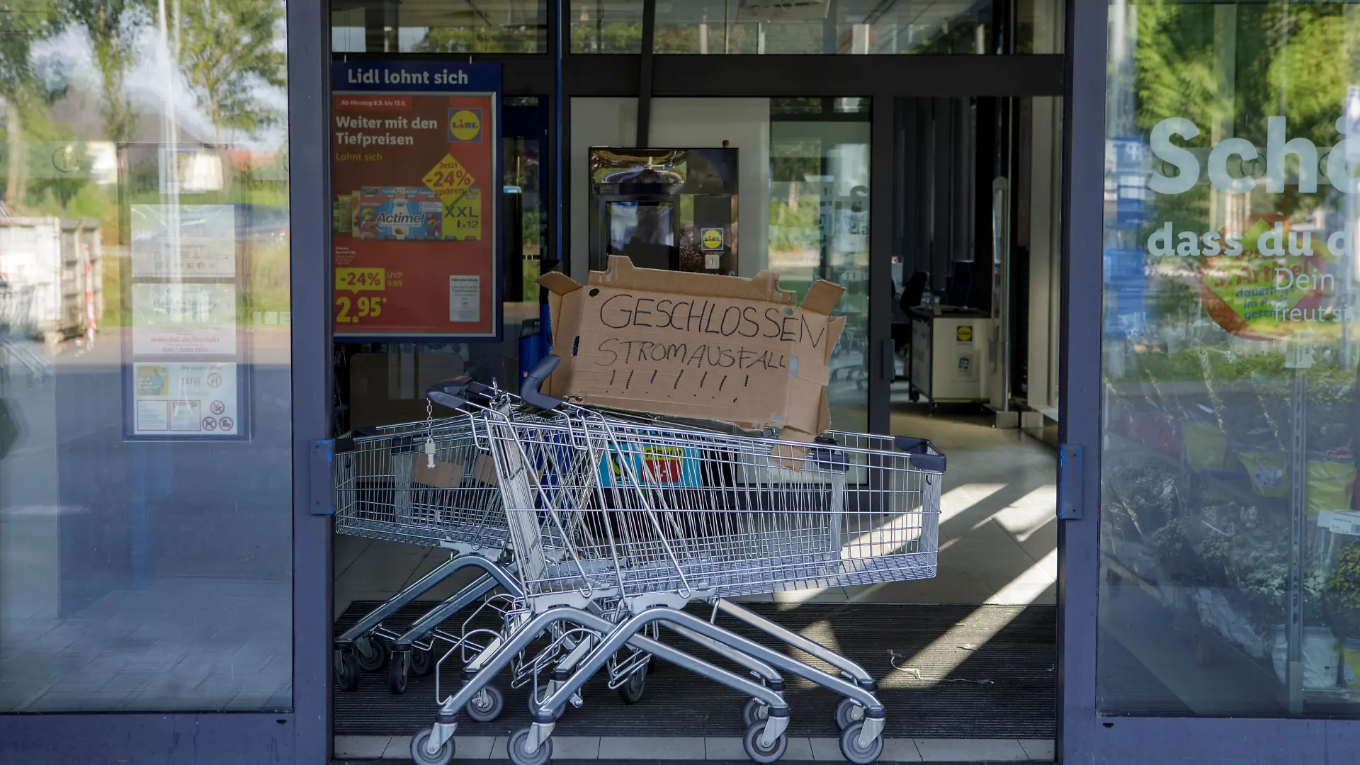 Im Eingang eines Supermarkts steht ein Einkaufswagen mit einer Pappe mit der Aufschrift „Geschlossen Stromausfall”. 