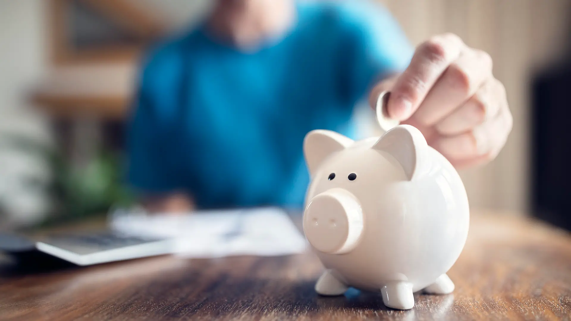 Man putting a coin into a pink piggy bank concept for savings and finance