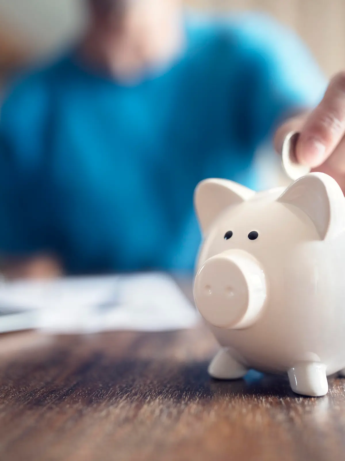 Man putting a coin into a pink piggy bank concept for savings and finance