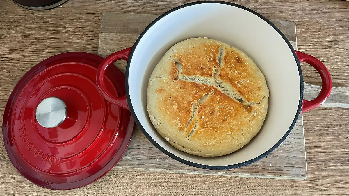 Roter Schmortopf mit frisch gebackenem Brot auf dem Herd. 