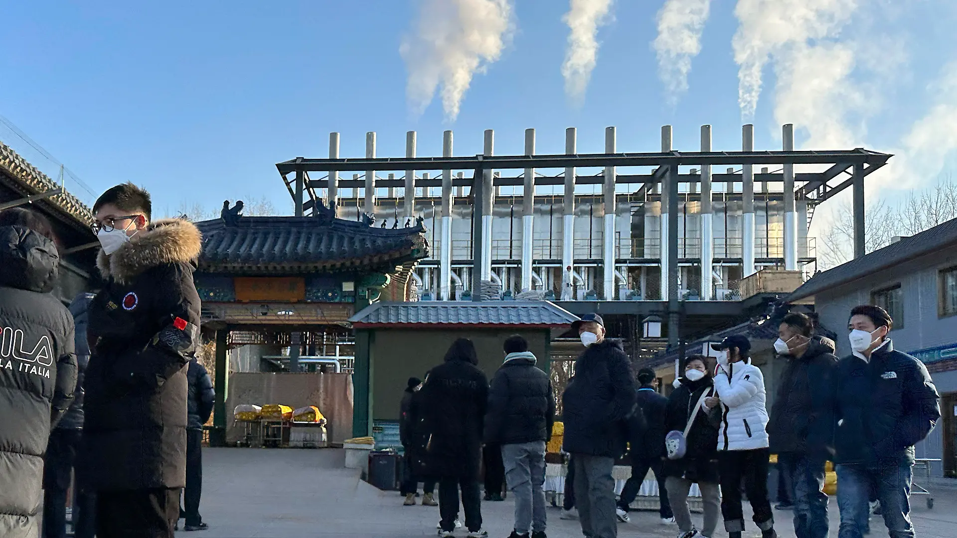 31.12.2022, China, Peking: Trauernde stehen vor einem Krematorium, während Rauchsäulen aus den Schornsteinen für die Einäscherung aufsteigen. China hat Anfang dieses Monats viele seiner strengen Corona-Beschränkungen aufgehoben, so dass sich das Virus rasch ausbreiten konnte. Die Zahl der Einäscherungen ist um ein Vielfaches gestiegen. Viele Bestattungsinstitute sind ausgelastet und bitten die Familien die Beerdigungen zu verschieben. Foto: Ng Han Guan/AP/dpa +++ dpa-Bildfunk +++