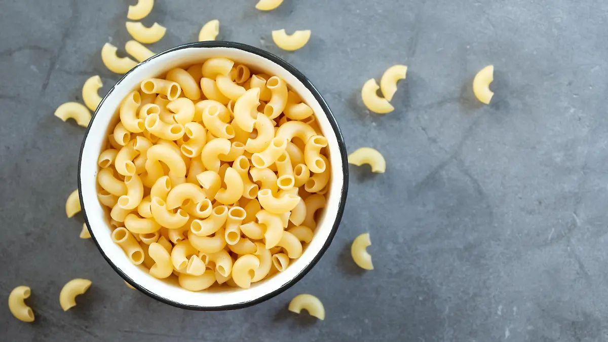 raw elbow macaroni in enamel bowl on dark cement table background.