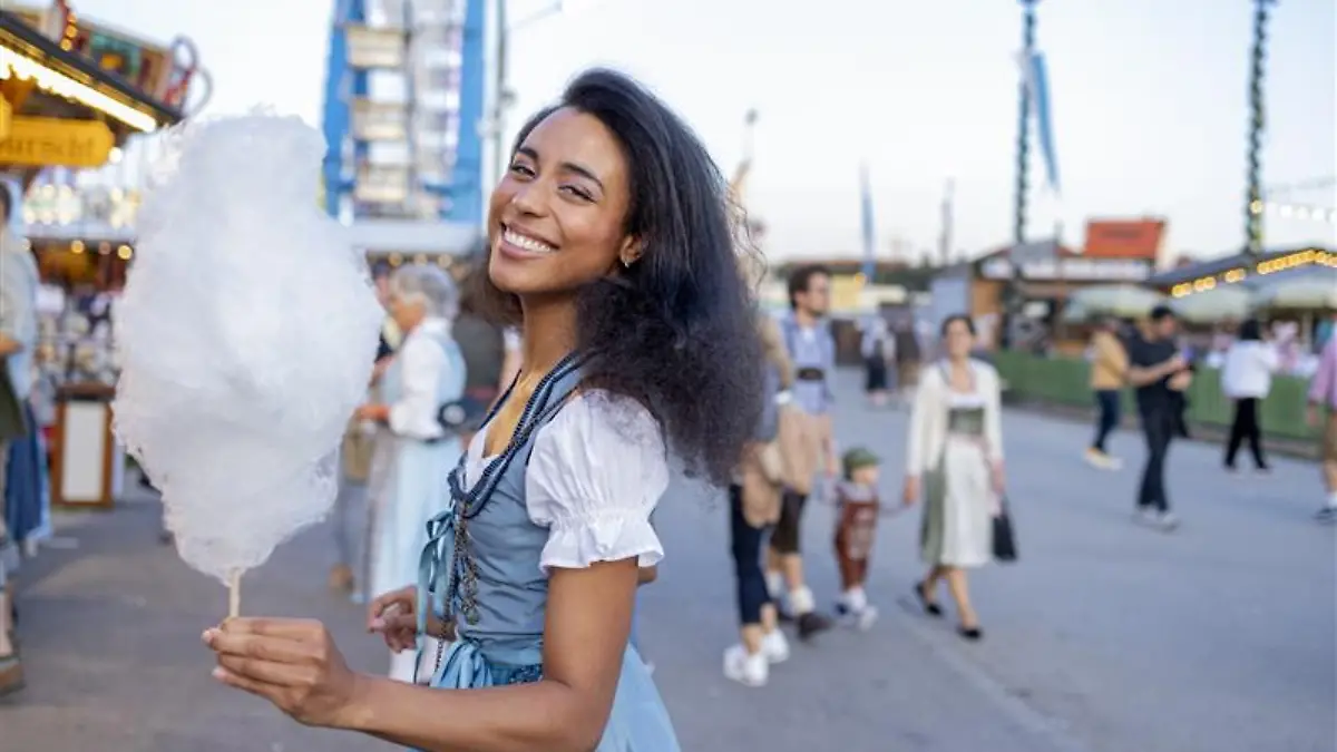 Frau in Dirndl isst Zuckerwatte und lacht.