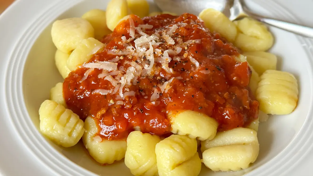 Gnocchi mit Sauce Bolognese, bestreut mit frisch geriebenem und halb geschmolzenen Parmesankäse und frischem Pfeffer