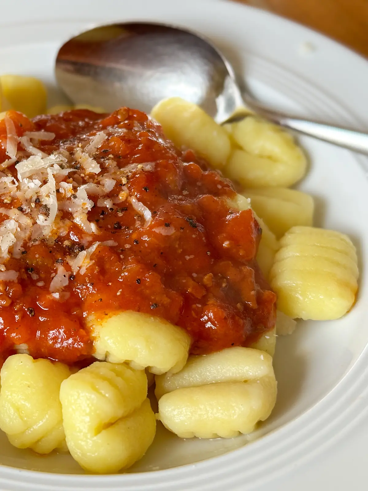 Gnocchi mit Sauce Bolognese, bestreut mit frisch geriebenem und halb geschmolzenen Parmesankäse und frischem Pfeffer