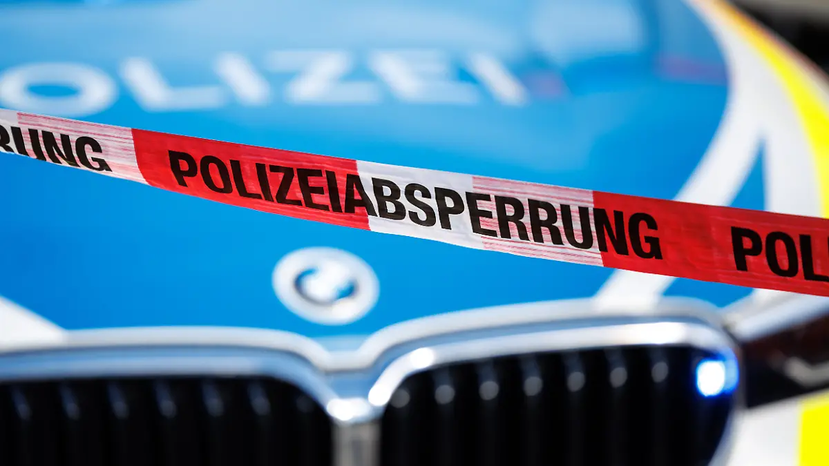 Flatterband mit der Aufschrift Polizeiabsperrung, im Hintergrund ein Einsatzfahrzeug der Polizei.