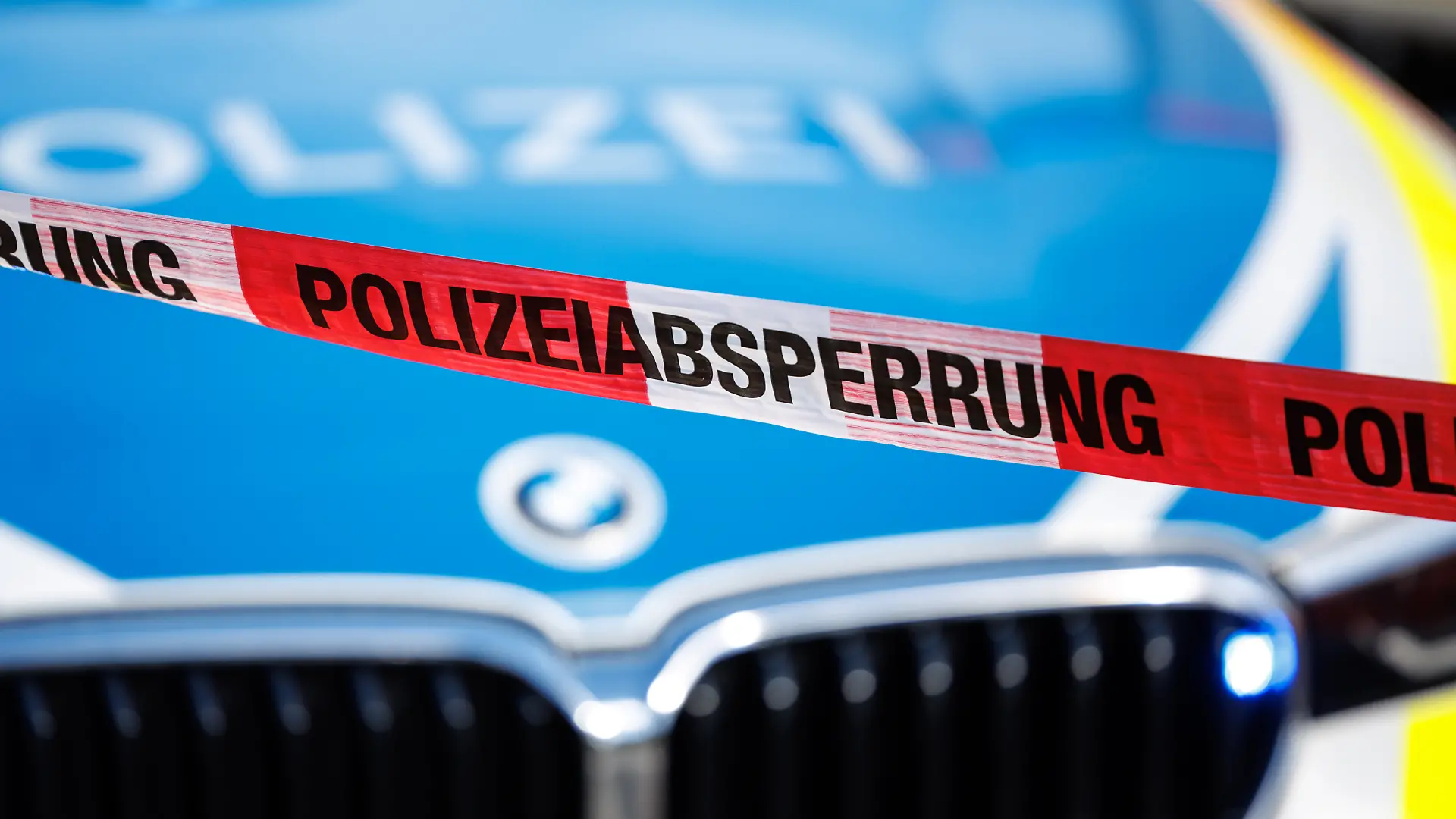 Flatterband mit der Aufschrift Polizeiabsperrung, im Hintergrund ein Einsatzfahrzeug der Polizei.