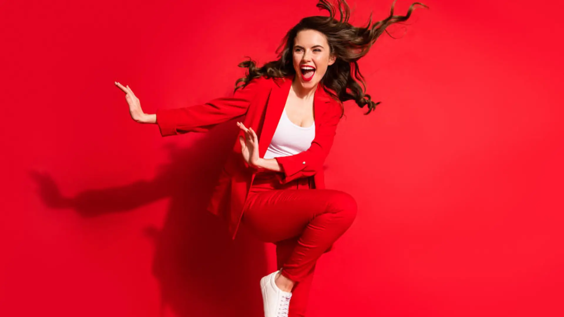 Full length photo of young girl wind blow hairdo raise knee look side empty space wear jacket pants footwear isolated red color background