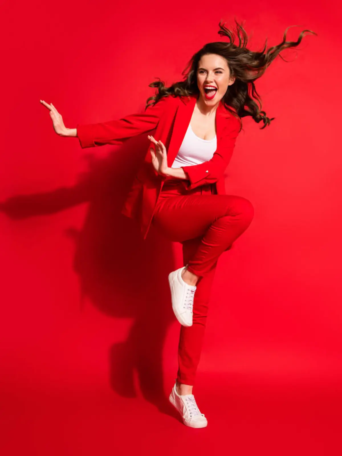 Full length photo of young girl wind blow hairdo raise knee look side empty space wear jacket pants footwear isolated red color background