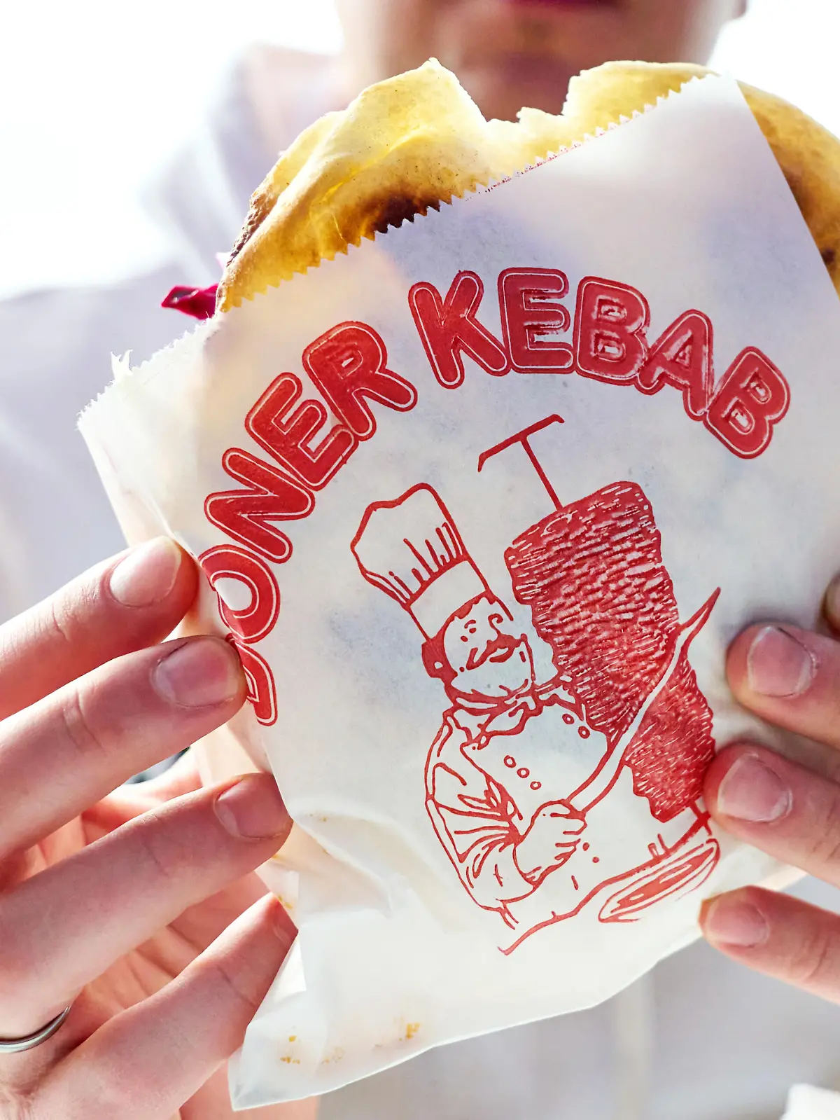 Mann hält einen Döner Kebab in einer bedruckten Dönerverpackung. Fastfoodgericht im Restaurant oder Imbiss. Typisches Streetfood mit Fleisch, Salat und Sauce.