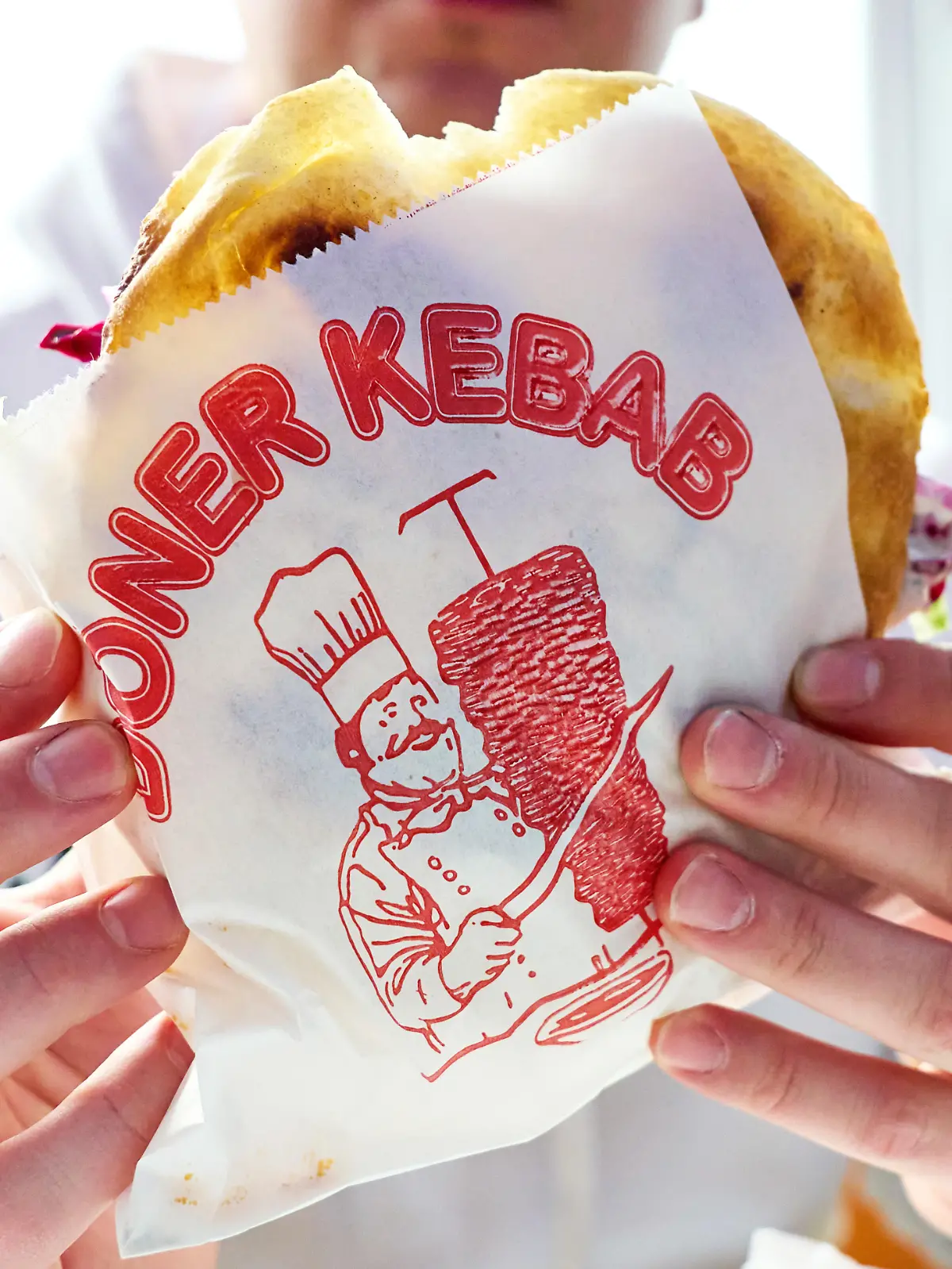 Mann hält einen Döner Kebab in einer bedruckten Dönerverpackung. Fastfoodgericht im Restaurant oder Imbiss. Typisches Streetfood mit Fleisch, Salat und Sauce