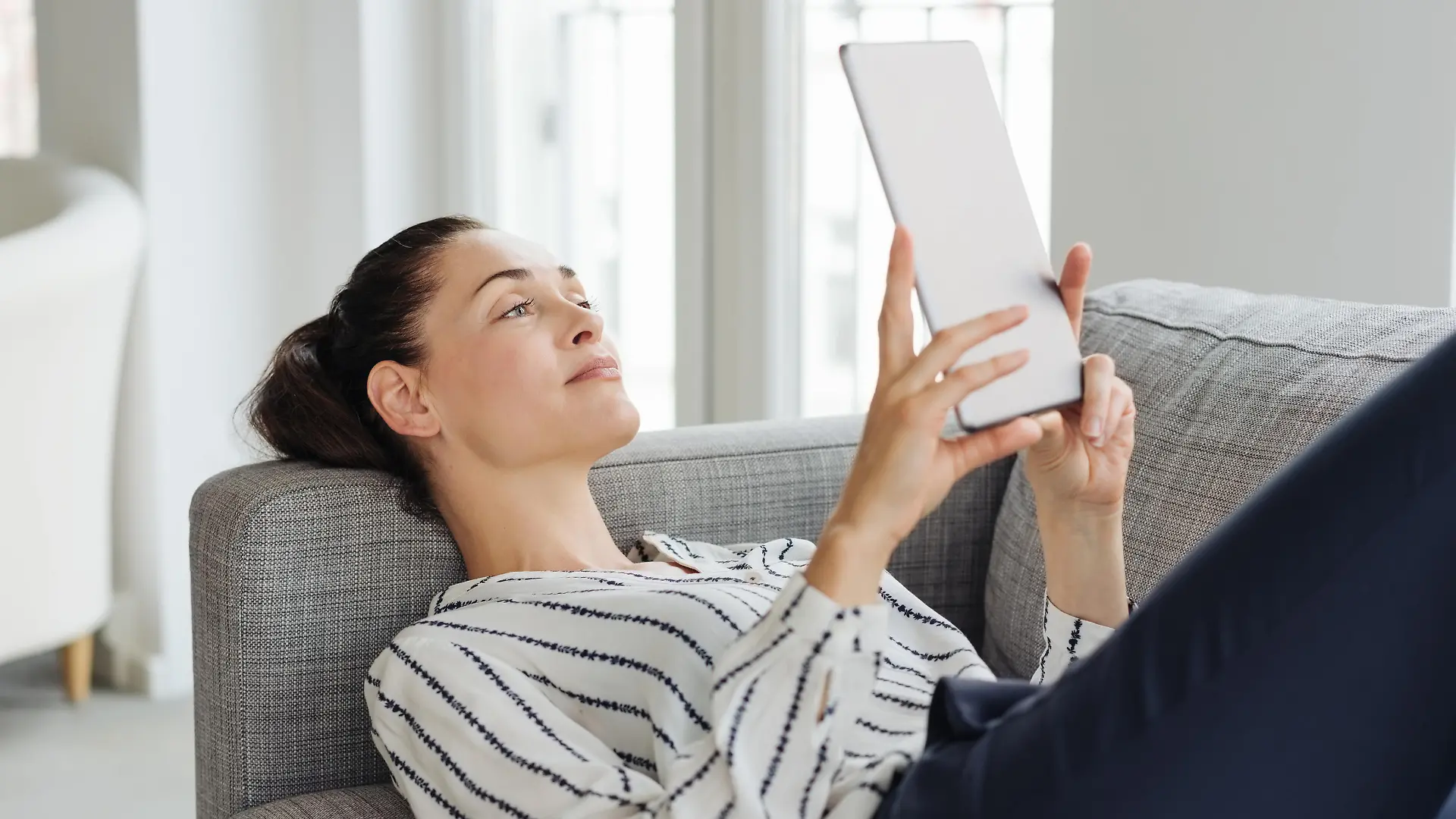 Young smiling woman using tablet while relaxing on sofa at home