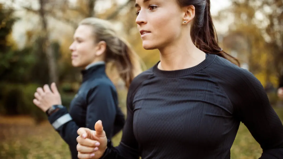 Fitness woman in sportswear running in the park with female at the back.  Female on morning run outdoors.